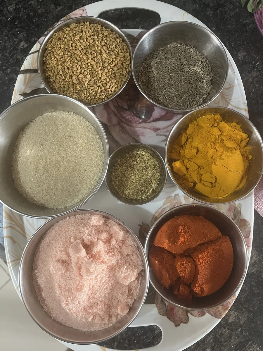 The ingredients of Awadhi Buknu in steel katoris: methi dana, jeera, raw cane sugar, ajwain, haldi, pink rock salt and red chilli